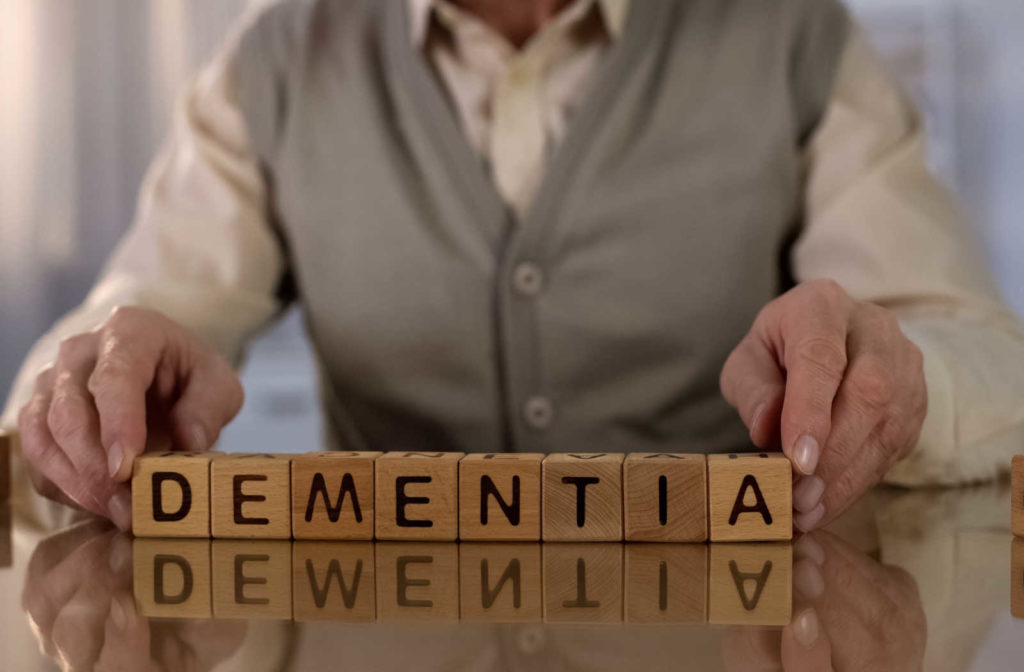A close-up photo of an elderly man's hand spelling out the word 'dementia' with wooden letters on a surface, his fingers are wrinkled with age, The word dementia indicating the man's illness or situation.