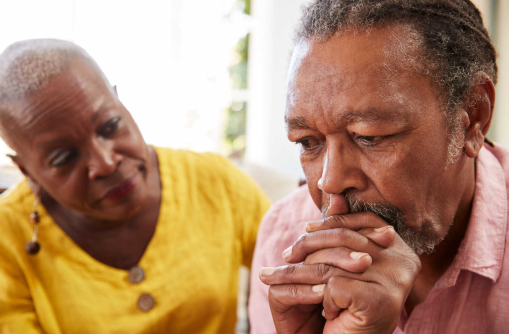 A photo of a senior woman consoling a man, who appears to be in depression, sitting next to him on a couch in a homely setting, the woman has a empathetic look and placed her hand on his shoulder, indicating support and care.