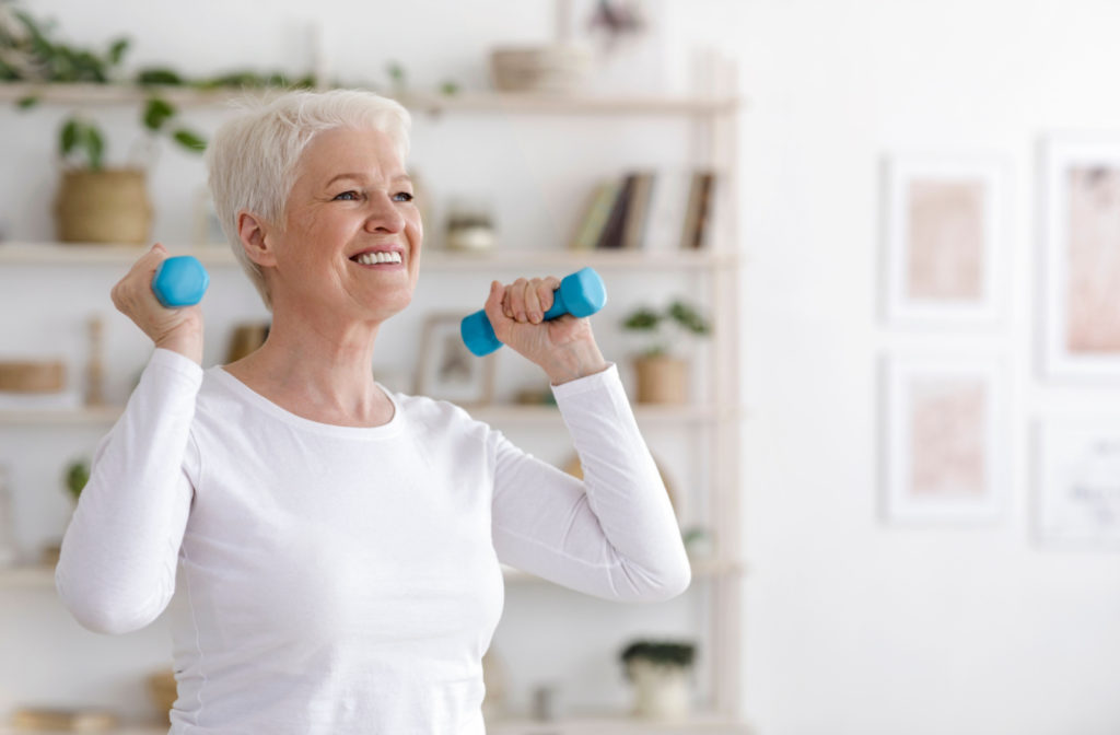 A smiling older adult woman exercising with dumbbells.