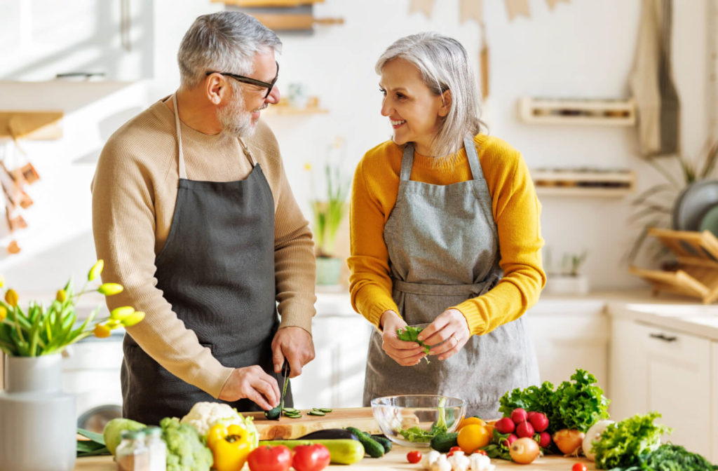 An older couple in a sunlit kitchen smiling and working together to make a nutrient-dense dinner for cognitive health.