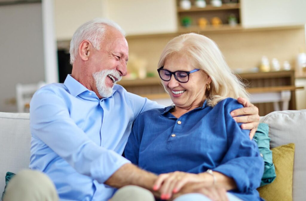 A senior couple cuddles lovingly on the couch in their home, laughing and enjoying each other’s company on a cold winter day