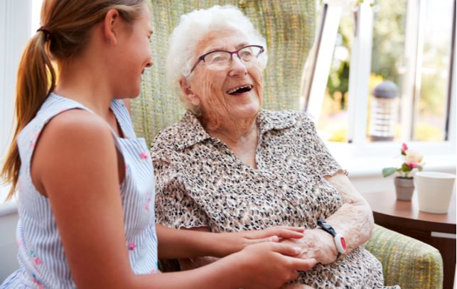 Happy senior women sitting in chair and talking to senior home nurse