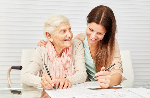 A young woman and an elderly woman solve a crossword puzzle together.