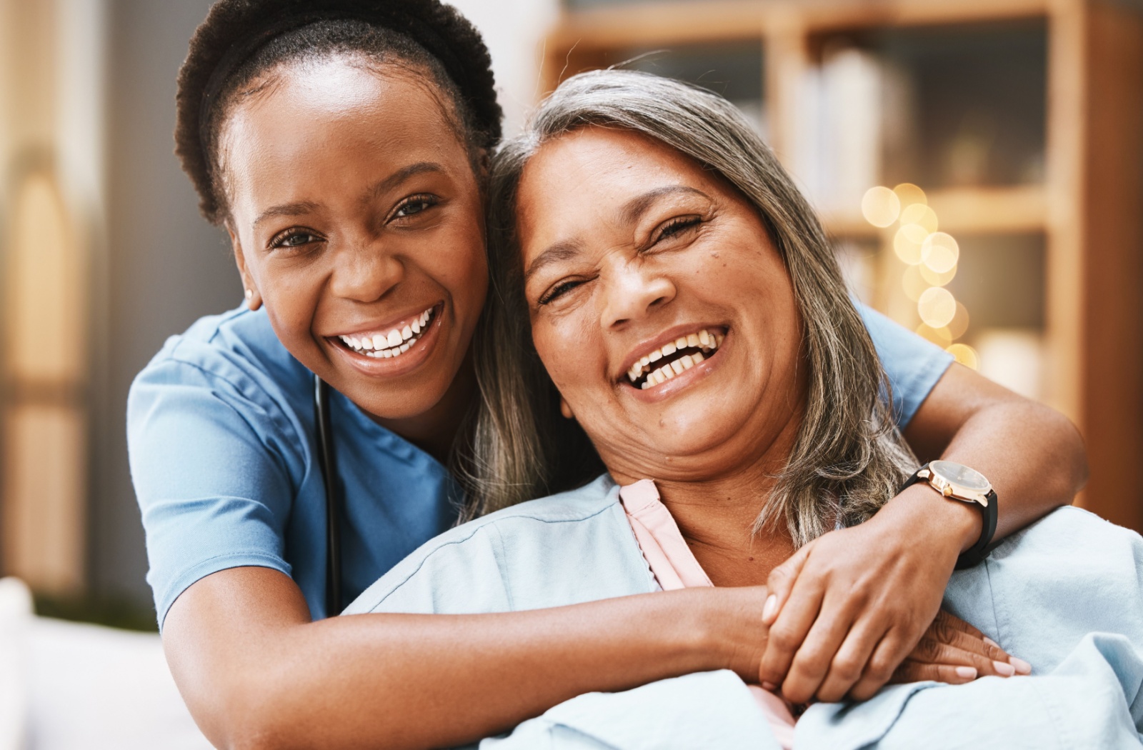 A nursing home staff hugging a resident from behind. Both of them smiling.