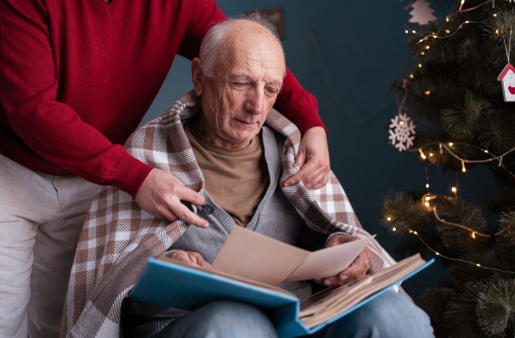 A mature adult reminisces through a photo album in the company of a loved one.