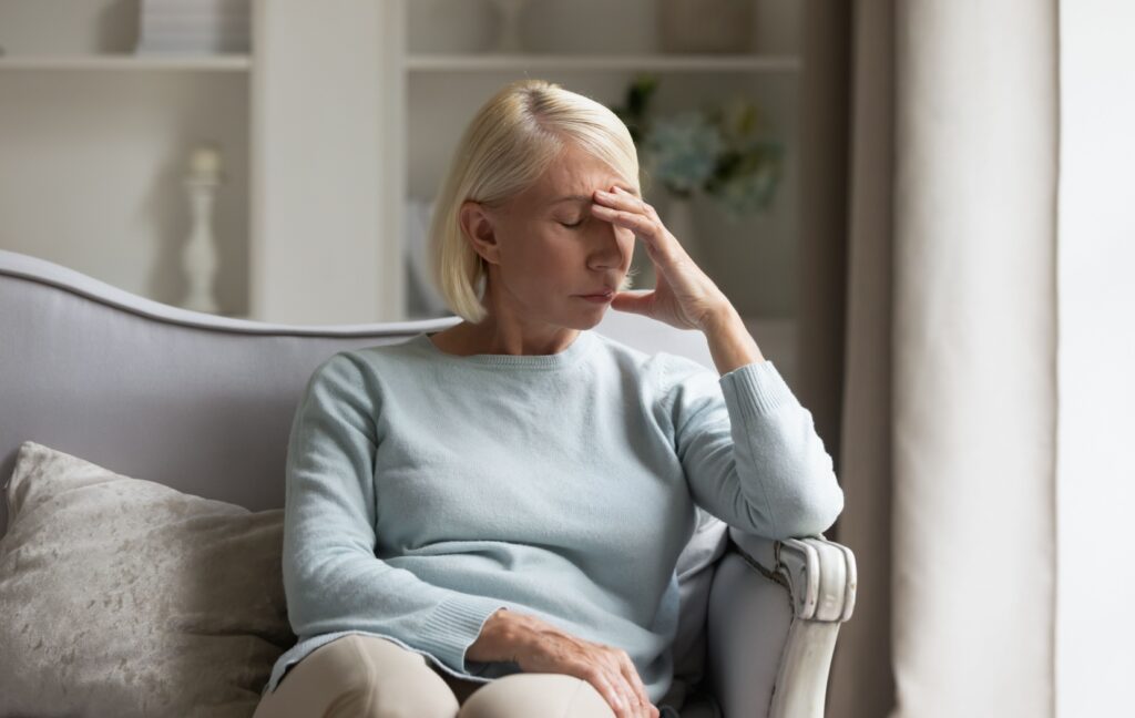 A tired and burnt-out caregiver sits alone and rubs their eyes over the stress of taking care of their senior loved one.