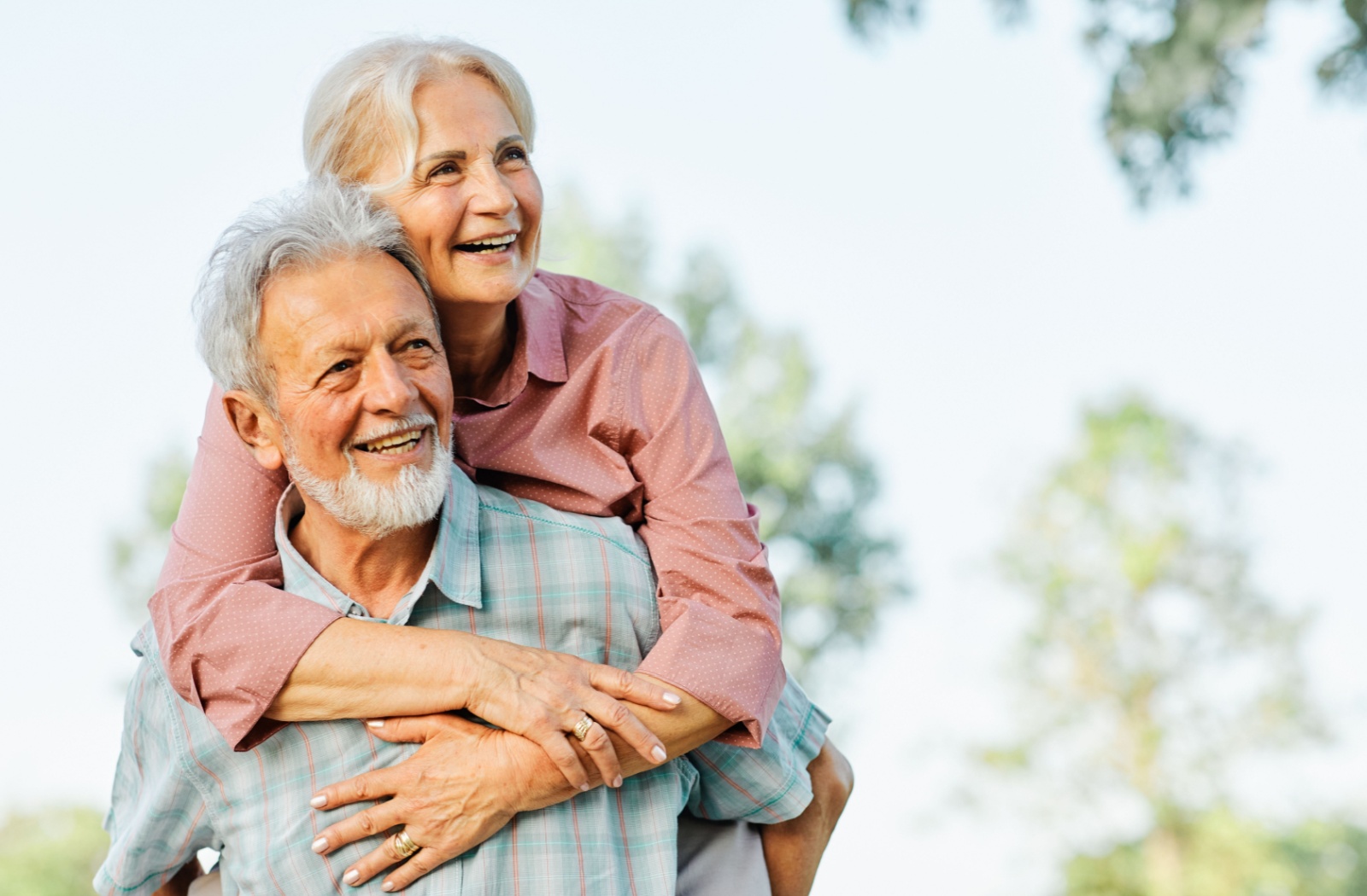 Two seniors enjoying a joyful moment outdoors, both smiling and embracing a positive outlook on life.