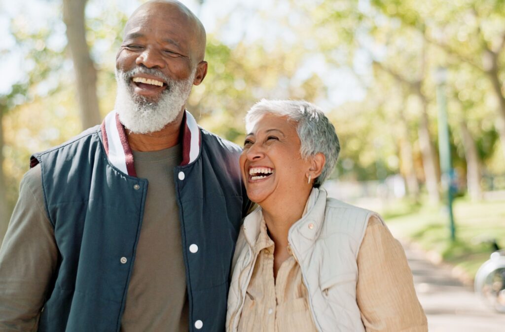 Two seniors laughing together outdoors, embodying a positive attitude towards aging.