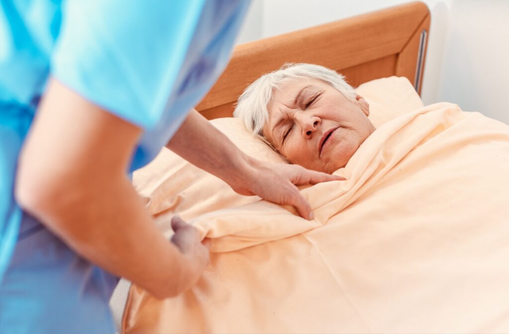 A nurse in memory care helps tuck a senior with dementia into bed after going through their bedtime routine.