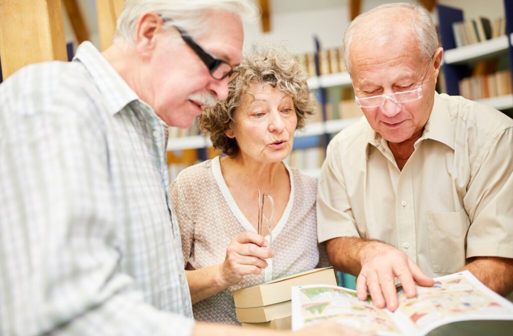 Three seniors look over several books while in a community library, trying to decide on a title to read for their book club.