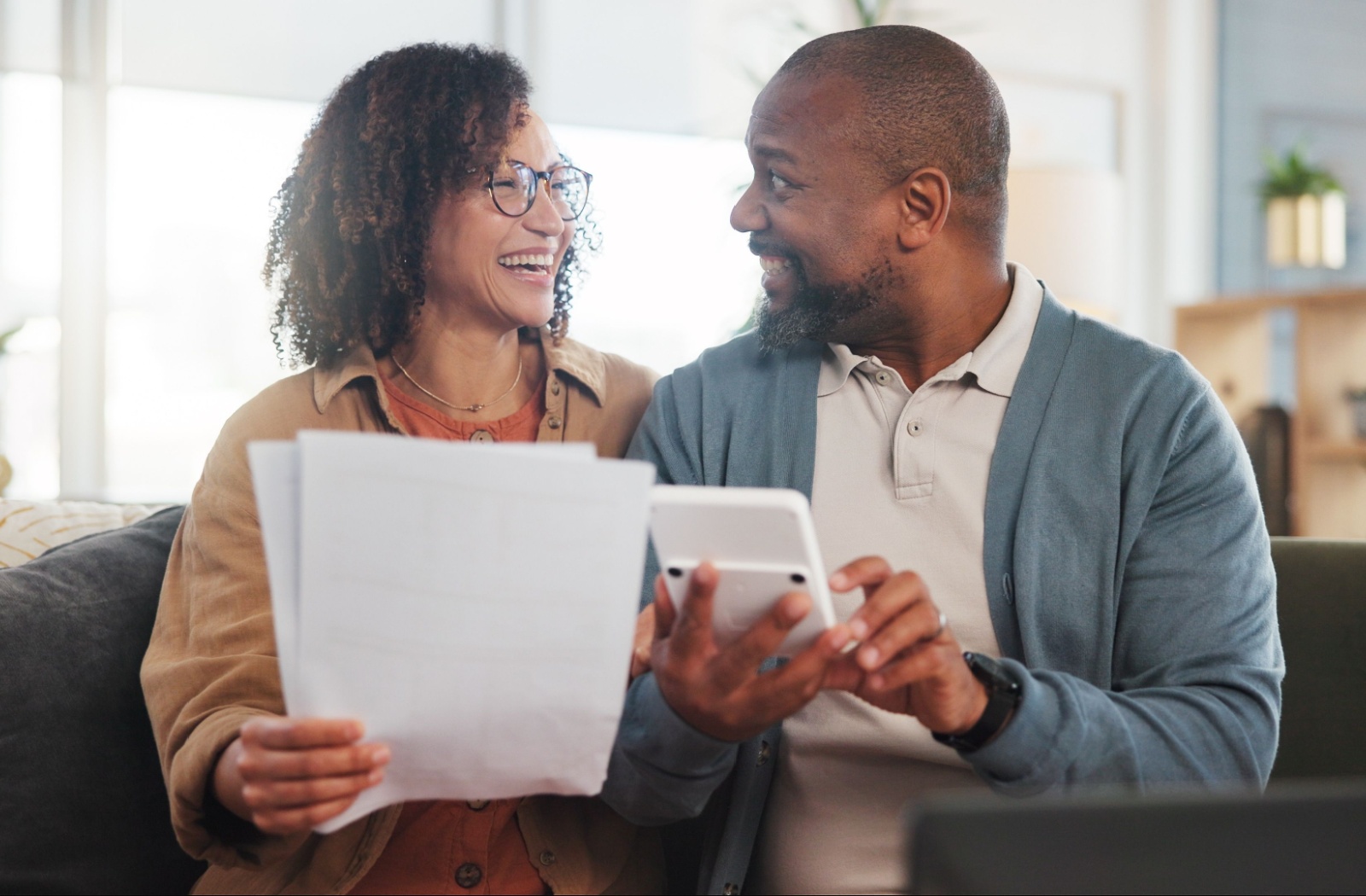 A couple planning for retirement laugh together in excitement upon realizing they have more saved than they thought.