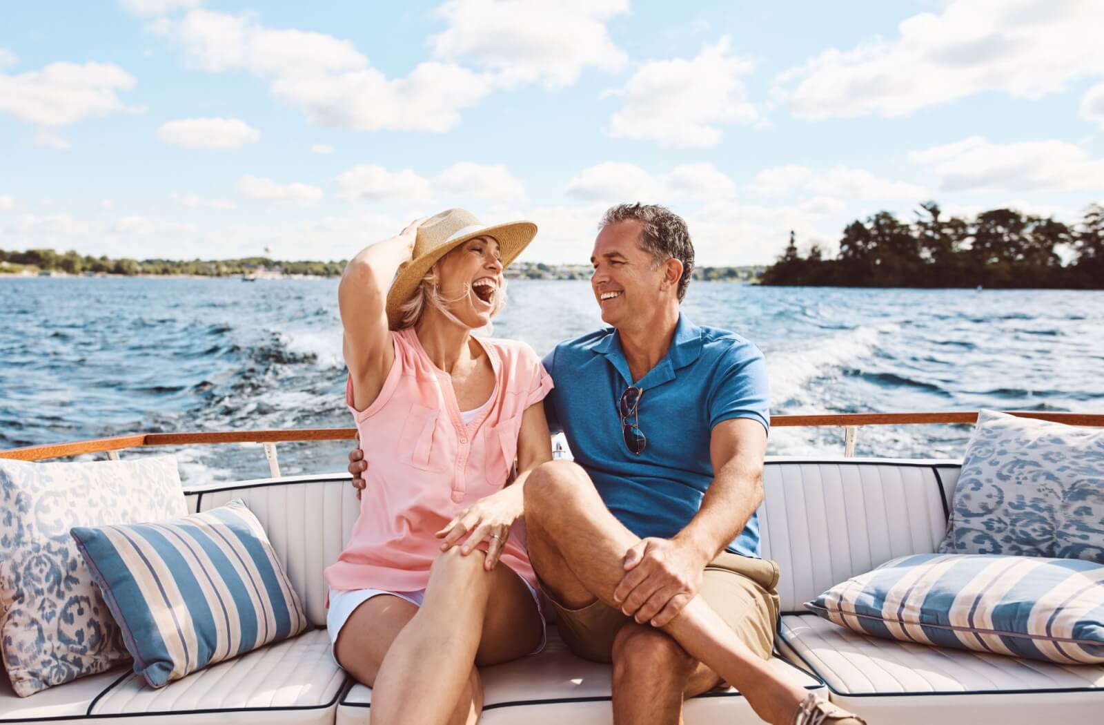 A newly retired couple sit on the back of a boat, enjoying a ride out on a lake on a beautiful summer day