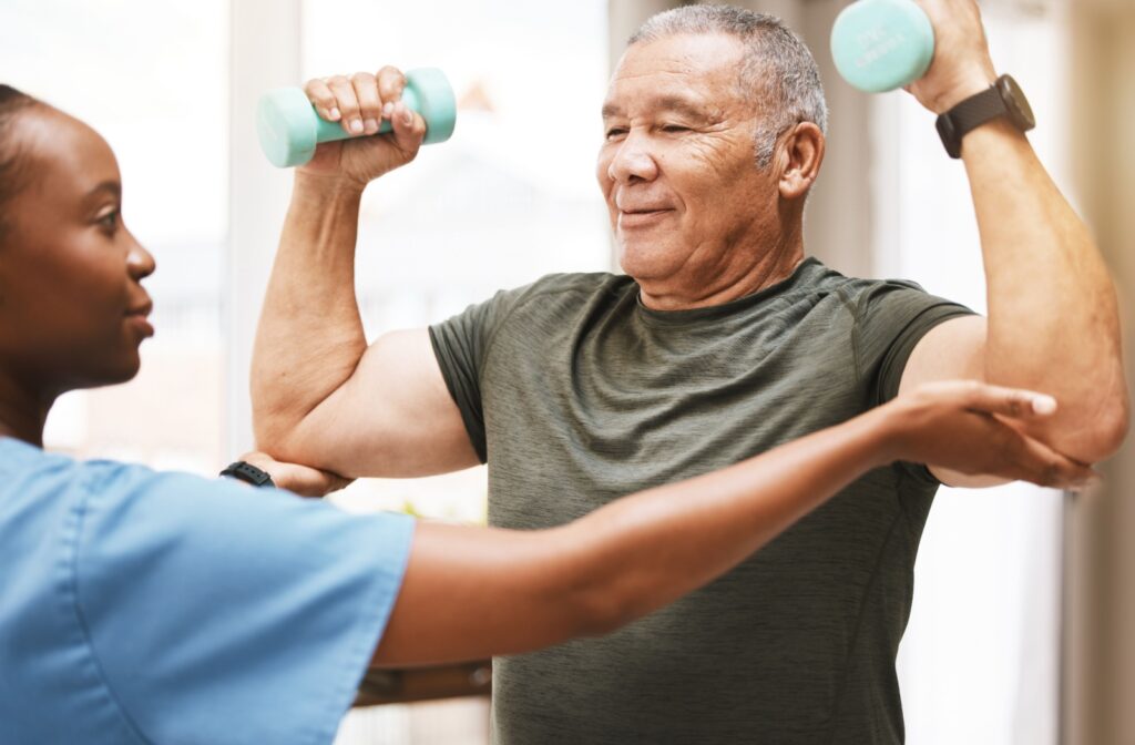 A caregiver assists a senior lifting weights.