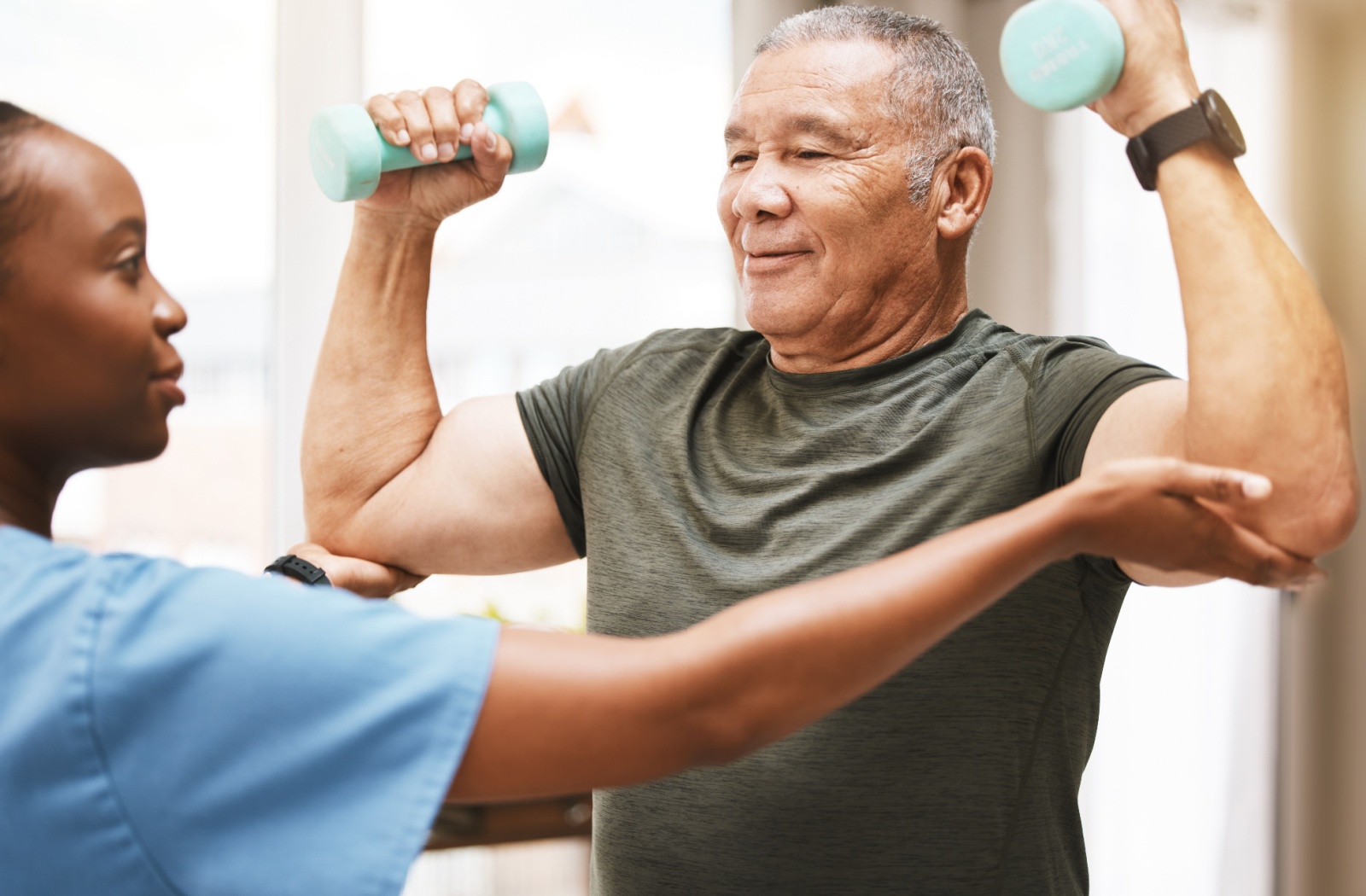 A caregiver assists a senior lifting weights.