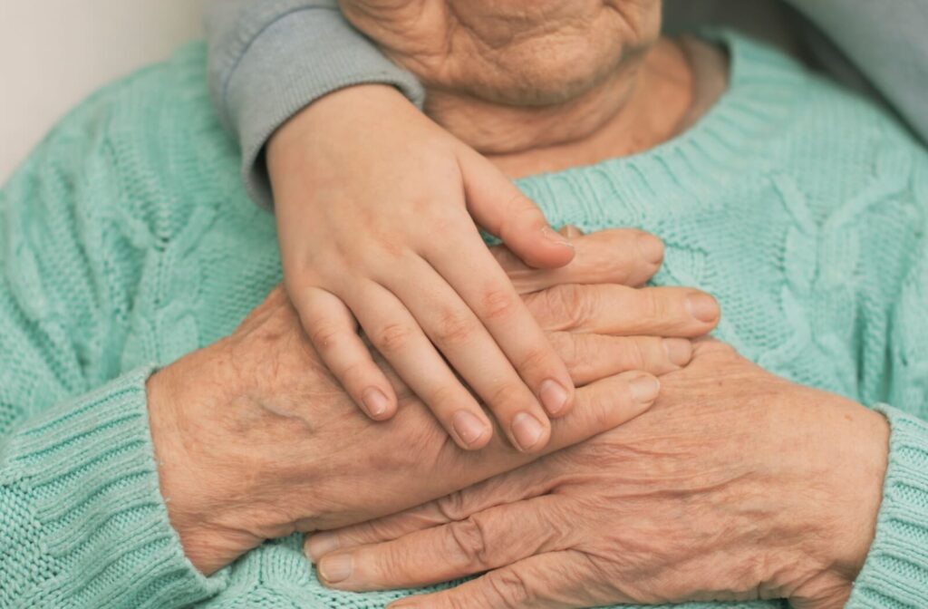 Close-up of younger and older hands together on chest symbolizing care support and connection across generations